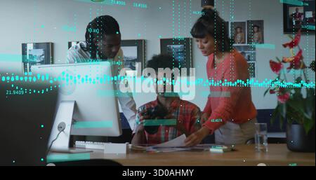 Leaning coworkers reviewing prints and camera at studio table, with monitor and potted plant Stock Photo