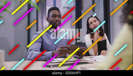 Blue-shirted man holding tablet guiding team discussion in conference room, with printed documents Stock Photo