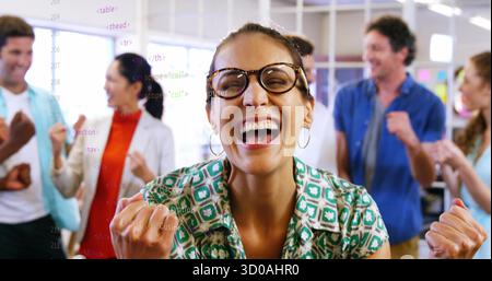 Cheering coworkers wearing glasses pumping fists in office, with code snippets on glass partition Stock Photo