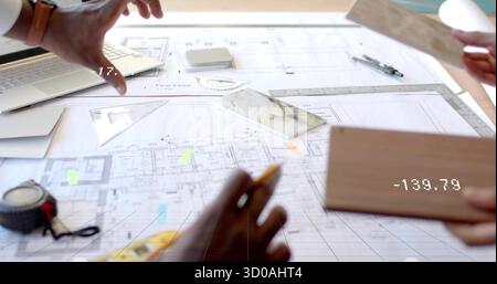 Architects examining floor plan blueprint in design studio, with laptop and tile samples Stock Photo