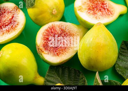 Ripe green fig fruits with fig leaves and fig pieces isolated on green background. Stock Photo