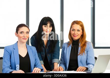 A trio of confident women stands together in a studio, showcasing diversity and professional style. They wear casual to smart-casual outfits, conveyin Stock Photo