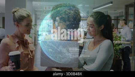 Three women reviewing content on laptop in open-plan office, with digital globe projection Stock Photo