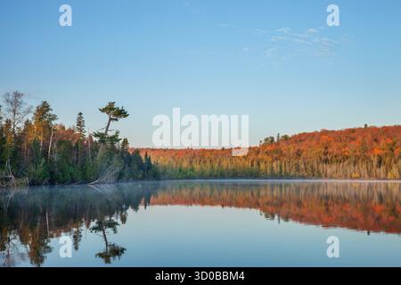 Beautiful calm northern Minnesota lake below hills in fall color on a clear autumn morning Stock Photo