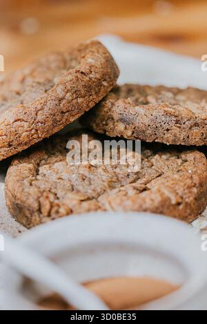 Three cookies stacked on top of each other on a white plate. The cookies are brown and have nuts on top Stock Photo