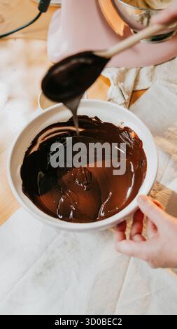A person is making chocolate sauce in a bowl. The sauce is poured into a white bowl. The person is holding a spoon and is pouring the sauce into the b Stock Photo