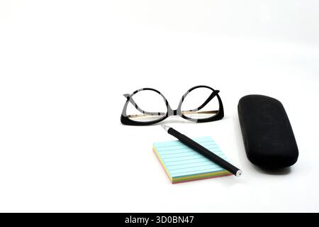 Pen on a pad of reminder notes with a pair of women's glasses and a glasses case isolated on a plain white background. Copy space. No people. Stock Photo