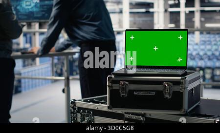Close up of isolated screen laptop in front of data center programmers improving AI rigs processing speed. Server hub coworkers manage gear using chroma key device to support AI workloads, camera B Stock Photo