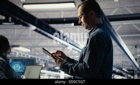 IT expert in server hub uses tablet to optimize deep learning AI systems handling tasks. Data center programmer adjusts artificial intelligence model parameters using device, camera B Stock Photo