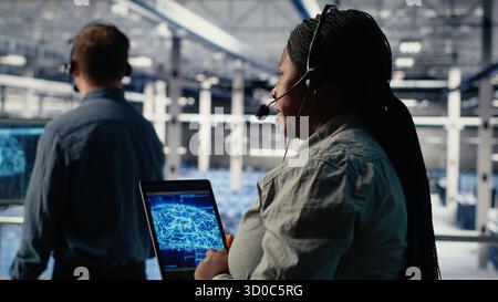 Team of data center programmers use AI to help customers resolve website hosting problems. Teamworking server farm tech support experts help users keep their online services running smoothly, camera B Stock Photo