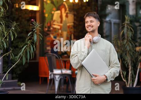 Young male programmer with headphones and laptop in street cafe Stock Photo