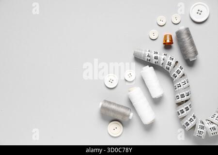 Thread spools with buttons, measuring tape and thimble on grey background Stock Photo