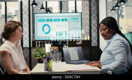 Human resources specialist evaluating the job application of a woman, discussing CV resume information during hiring interview, asking questions to ensure a successful meeting for employment. Camera B. Stock Photo