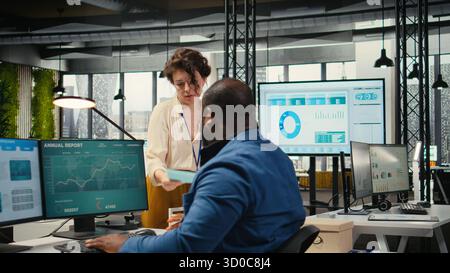 Workplace support employee moves a delivery cart stacked with folders and contracts, helping african american administrator bringing stack of archived documents for accounting tasks. Stock Photo