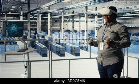 Data center IT expert investigates AI configurations using virtual reality, making adjustments for optimal function. Server hub engineer checks artificial intelligence error using VR headset, camera A Stock Photo