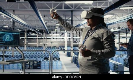 Software developer in server room wearing VR goggles optimizing deep learning systems handling tasks. African american woman in data center adjusts AI model parameters using virtual reality, camera A Stock Photo