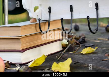 Antique key hanging on a rustic hook, surrounded by old books and autumn leaves, creating a nostalgic and cozy atmosphere Stock Photo