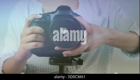 Adjusting DSLR camera on tripod, photographer in dotted shirt framing shot in studio, with flare Stock Photo