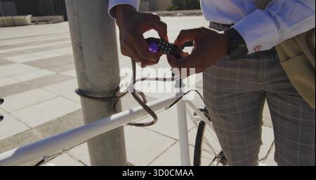 Commuter man in blue shirt locking white bicycle with cable lock in urban plaza, copy space Stock Photo