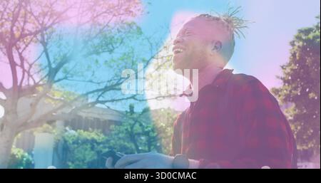 Smiling man with dreadlocks wearing red shirt holding smartphone in tree-lined quad, copy space Stock Photo
