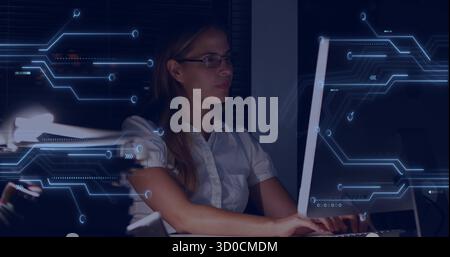 Monitoring woman in white blouse viewing circuit overlays on monitor in office at night, with lamp Stock Photo