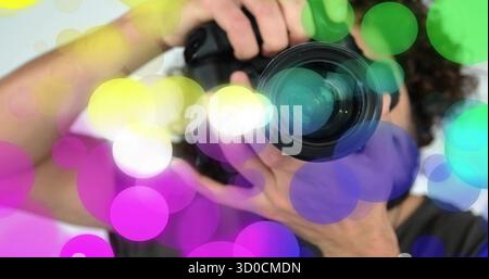 Holding DSLR camera photographer adjusting lens in studio, with lens cap and colorful bokeh overlay Stock Photo