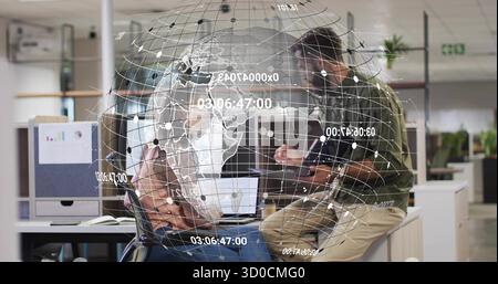 Collaborating colleagues tapping tablet and pointing at laptop screen in office, under data globe Stock Photo