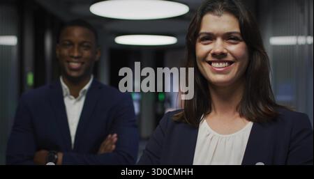 Smiling woman in navy blazer standing in office corridor, with overhead lights, glass walls Stock Photo