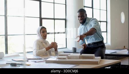 Collaborating architects discussing scale model at design studio table, with blueprints and laptop Stock Photo