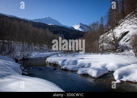 Winter mountain landscape with stream and snow-covered peaks in Val Müstair (Switzerland) Stock Photo