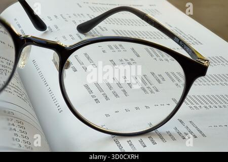 Close-up view of reading glasses resting on an open book filled with numerical data and text. The scene captures the essence of studying or analyzing Stock Photo
