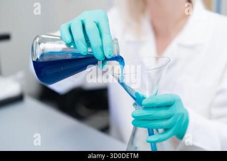 Female researcher carefully transferring liquid using a glass funnel during a chemical experiment in the laboratory. Concept of precision, scientific research, and clean working environment. Stock Photo