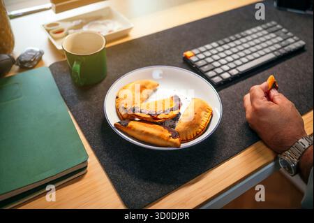 Plate with empanadas on desk beside keyboard and mug. Stock Photo