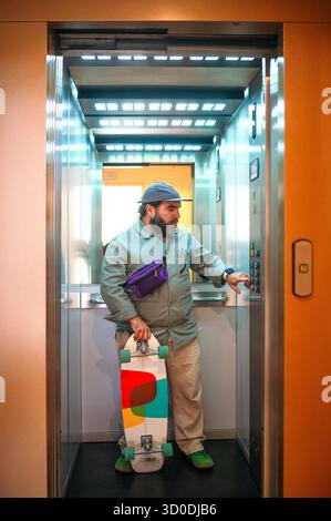 Man holding skateboard inside elevator pressing button. Stock Photo