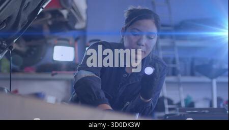 Coverall clad mechanic examining engine under hood in repair garage, holding flashlight Stock Photo