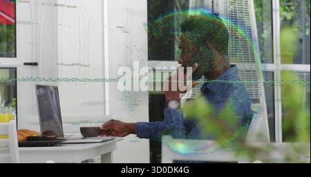 Sitting man wearing denim shirt talking on smartphone while typing on laptop at patio, copy space Stock Photo