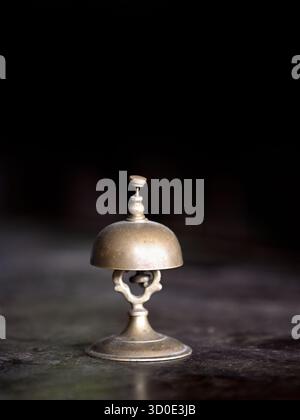 Vintage brass  hotel clerk service bell on wooden desk against dark background Stock Photo