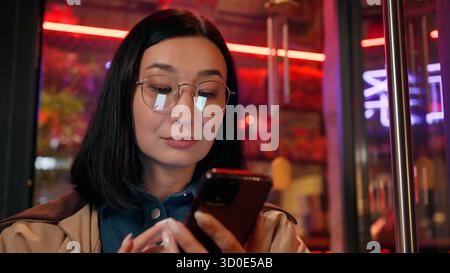 Japanese business woman female girl Korean businesswoman use mobile phone online map GPS app smartphone travelling outside city neon store. The Stock Photo