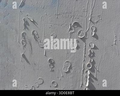 Peeling white paint forms abstract, circular shapes and bubbles on a textured wall, casting distinct shadows in the harsh light. Stock Photo