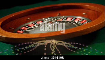 Spinning wooden roulette wheel rotating on green felt gaming table, with metal spindle assembly Stock Photo