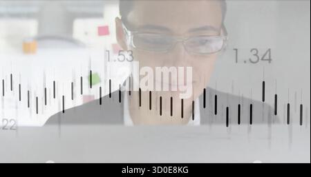 Analyzing woman wearing glasses reviewing financial chart at office desk with laptop, sticky notes Stock Photo