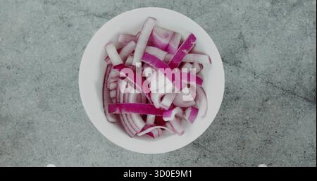Displaying white bowl containing thinly sliced red onion rings and strips on grey kitchen counter Stock Photo