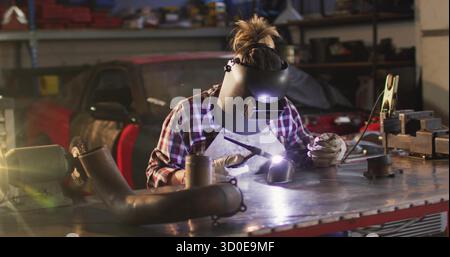 Female welder welding metal pipe sections at repair workshop, with welding torch arc and elbow pipe Stock Photo