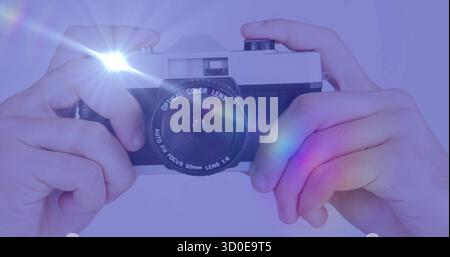 Holding vintage rangefinder camera to eye on purple backdrop, firing flash producing rainbow flares Stock Photo