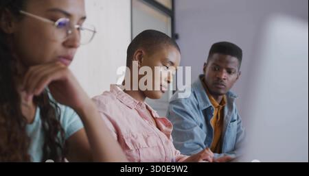 Writing woman in pink button-up shirt taking notes in study room at desk, with notebook laptop Stock Photo