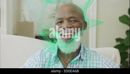 Senior man wearing plaid shirt viewing green hologram on sofa in living room, with curtains, plant Stock Photo