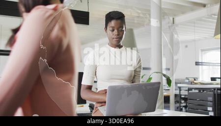 Focusing woman in white top and brown skirt typing at open-plan office desk, with laptop Stock Photo