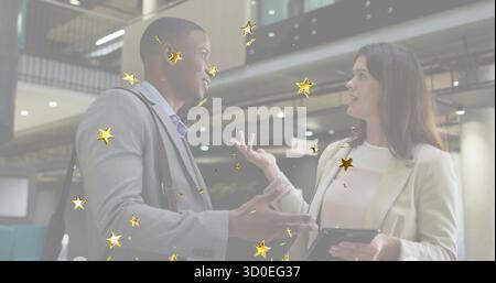Discussing two professionals reviewing project on tablet in office atrium, golden star overlays Stock Photo
