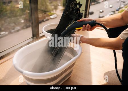 Close-up of unrecognizable cleaning service employee washing air conditioner filter with steam cleaner, focusing on maintenance and cleaning tasks Stock Photo