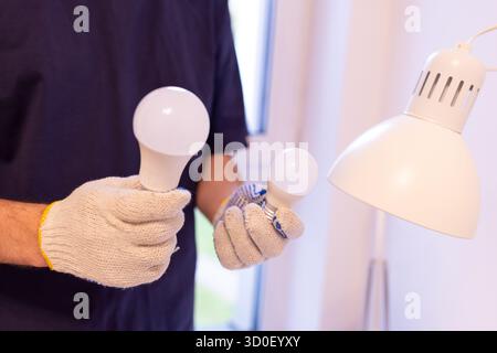 two light bulbs with different bases:E14 and E27. Concept of choosing the right bulb size.Close-up of hands in protective glove performing maintenance Stock Photo